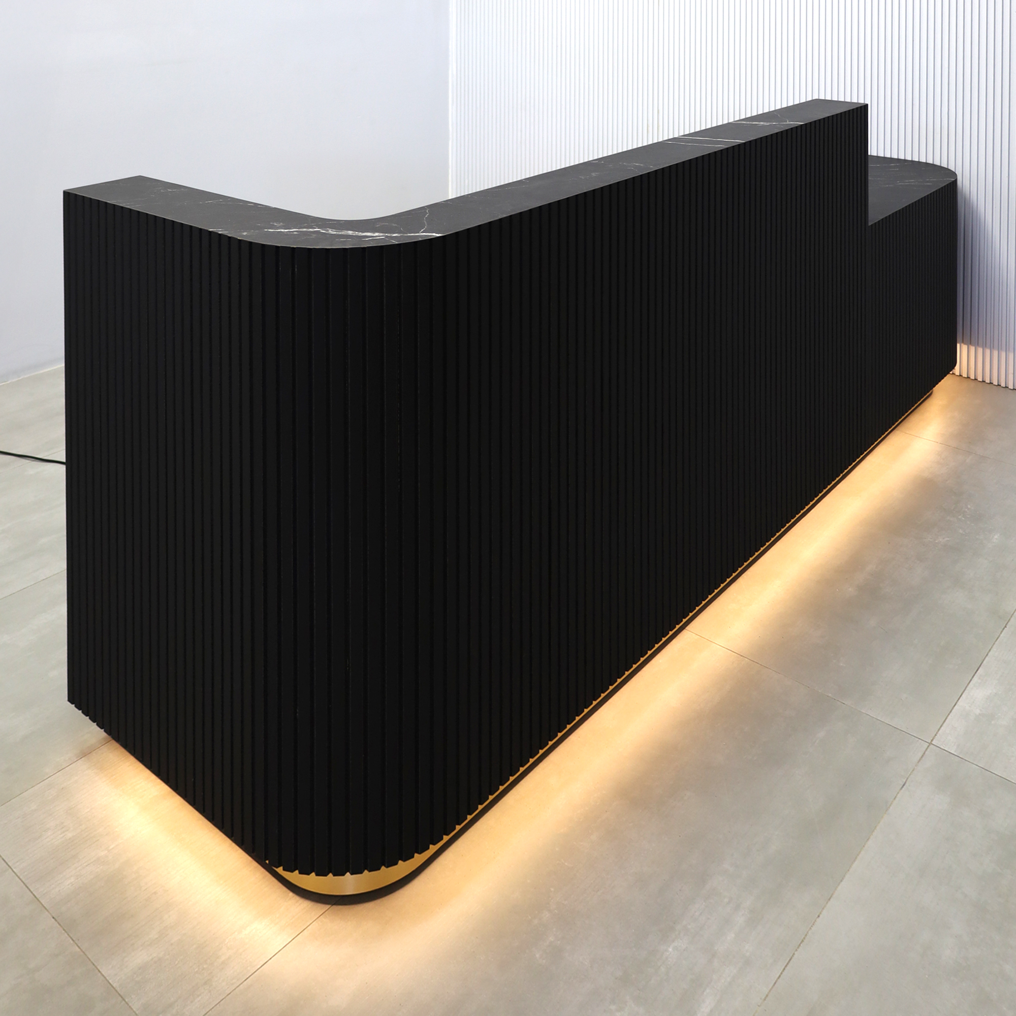 108-inch Nola ADA Reception Desk with Black traceless laminate tambour counter & desk, Black Stone Palazzo laminate workspace, gold aluminum toe-kick, warm white LED. 