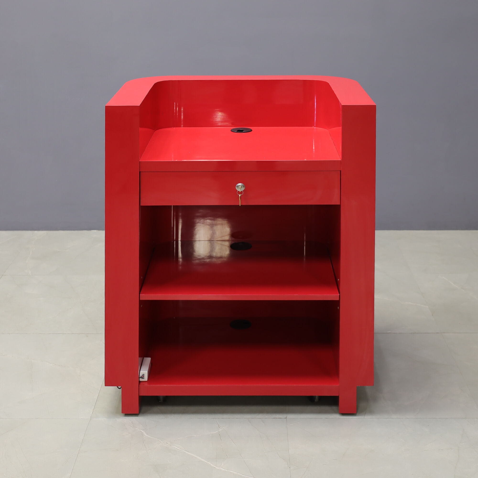 32-inch Nola Podium & Host in classic red gloss laminate main desk, brushed aluminum toe-kick, and warm white LED. Built-in pencil drawer with lock, one adjustable shelf and one fixed shelf.