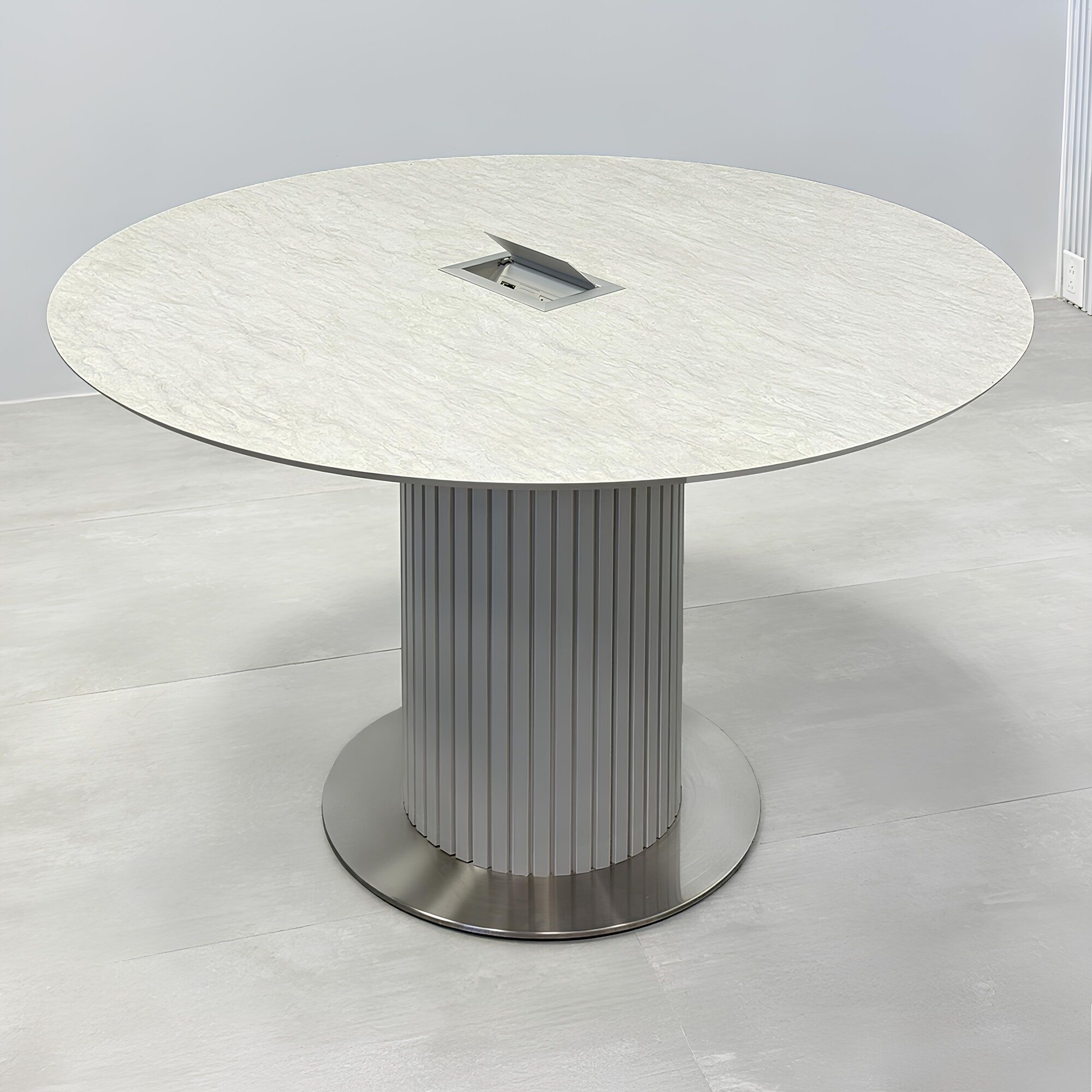 47-inch Aurora Round Conference Table with spanish limestone engineered surface top, fog gray tambour pedestal base, brushed stainless steel base, and Mx3 power box in silver.